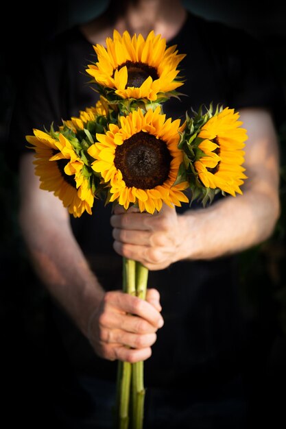 Foto close-up di una mano che tiene un fiore giallo su uno sfondo nero