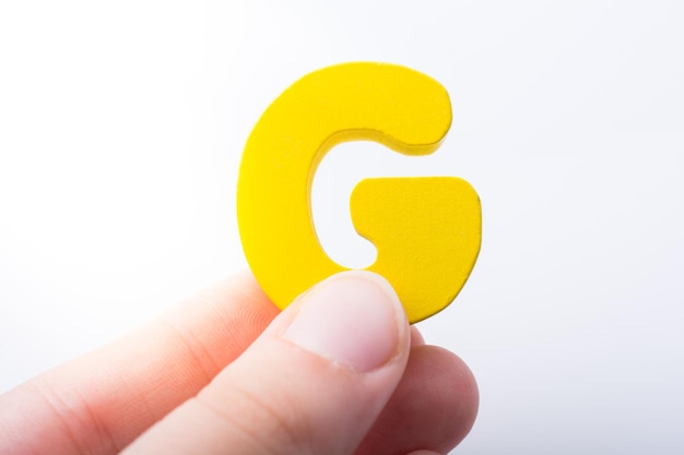 Photo close-up of hand holding yellow g against white background