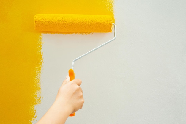 Close-up of hand holding yellow paint against wall