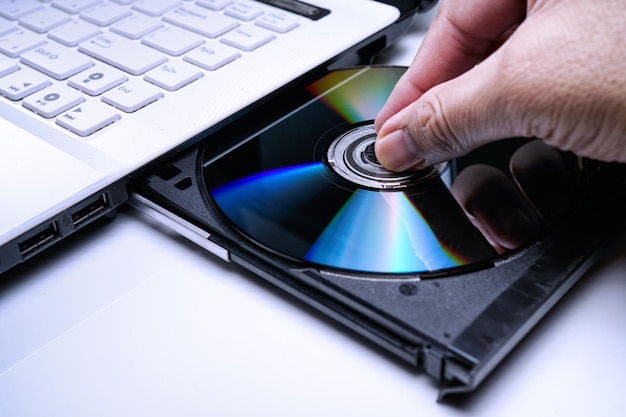 Photo close-up of hand inserting compact disc in laptop on table