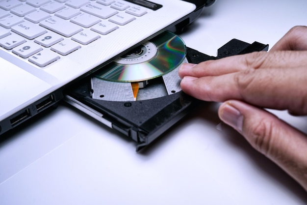 Foto close-up della mano che inserisce un compact disc in un portatile sul tavolo