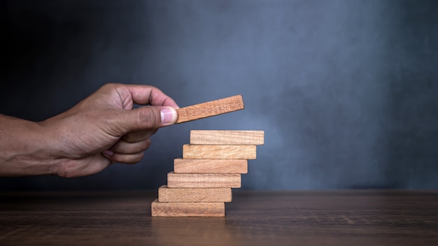 Foto la mano ravvicinata sta posizionando una torre di blocchi di legno impilata sul gradino delle scale