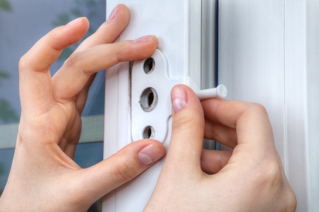 Close-up of hand of locksmith installing window limiter on plastic frame.