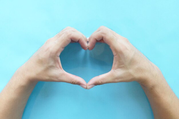 Photo close-up of hand making heart shape against blue background