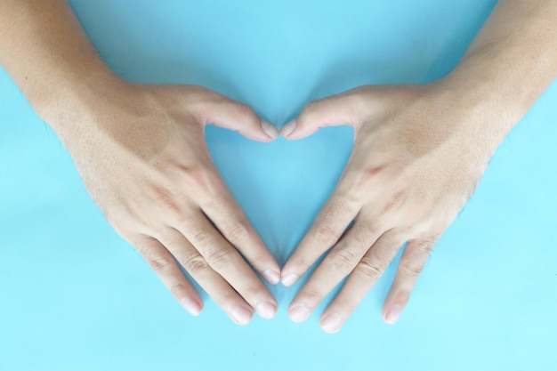 Close-up of hand making heart shape against blue background