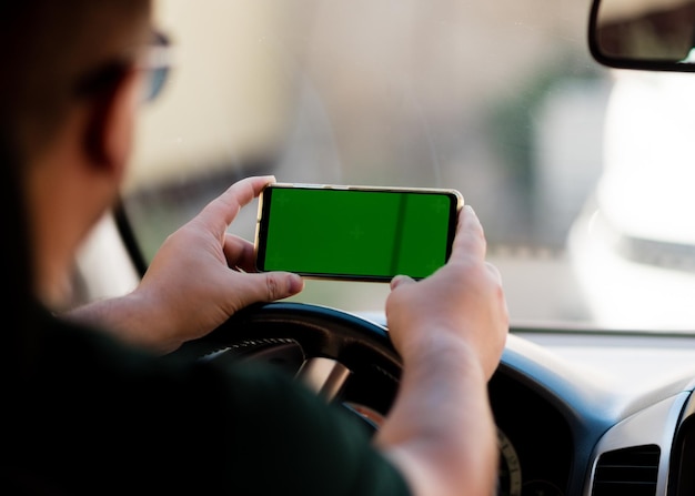 Крупным планом рука человека с помощью смартфона с зеленым экраном за рулем автомобиля. Путешествовать.