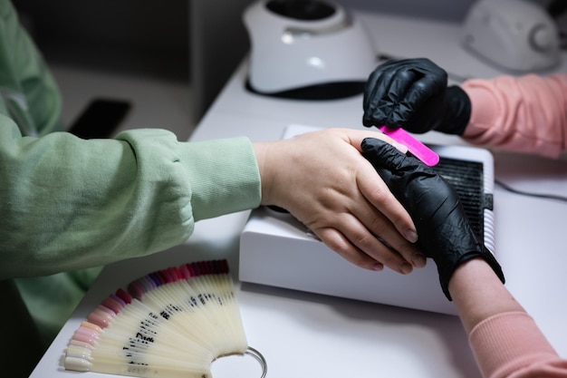 Close up hand of manicure master working with female client in beauty salon Manicurist makes woman nail