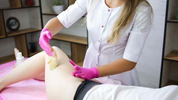 Close-up of the hand of the master who applies sugar paste on the client's thigh