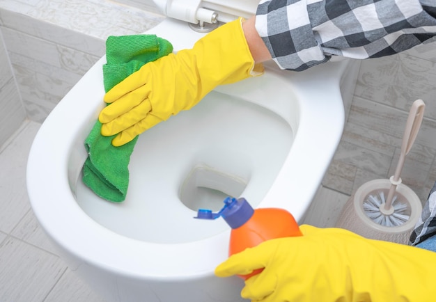Close-up hand met wasmiddel schoonmaak toilet Schoonmaakservice bijgesneden handen dragen gele beschermende handschoen met behulp van vloeibare reinigingsoplossing reiniging doorspoelen toilet desinfectie en hygiëne concept