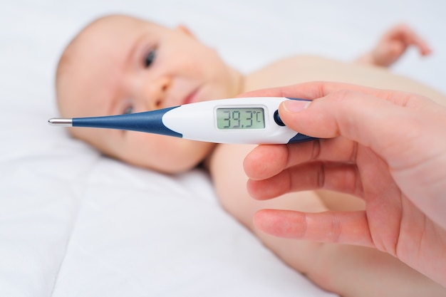 클로즈업 - 우는 아기의 배경에 39.3도 표시가 있는 온도계를 들고 있는 어머니 또는 의사의 손. 어린이 질병, 높은 체온.