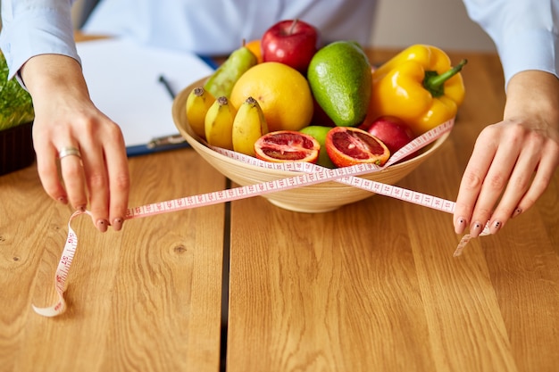 Close up of hand Nutritionist, dietitian workplace, woman hold measuring tape and measuring bowl with healthy vegetables and fruits, healthcare and diet, right nutrition and slimming wellness concept.