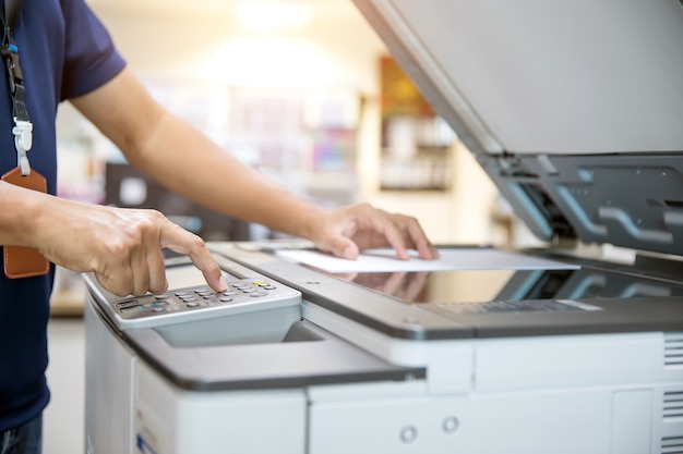 Close up hand of office man is press button on panel and put paper on the copier.