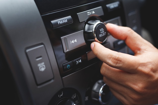 手を開いてカーラジオを聞いてクローズアップ。車の運転手が自分の車両マルチメディアシステムの回転ボタンラジオ局を変更する。最新のタッチスクリーンオーディオステレオシステム。輸送と車両のコンセプト