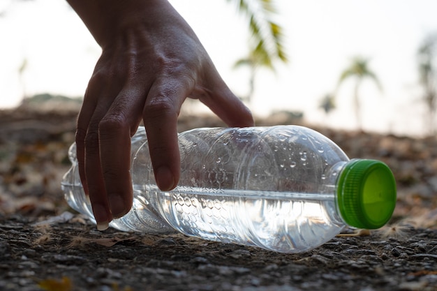 Close-up hand oppakken van doorzichtige plastic fles waterdrank met een groene dop op de weg in het park