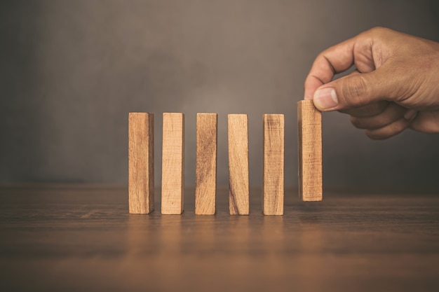 Close-up hand plaatst houten blok toren voorzichtig om vallende domino te voorkomen