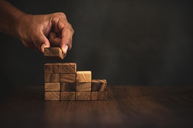 Close-up hand placing wood block tower stacked in stair step.