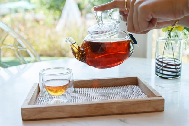 Photo close up of the hand pouring green tea from glass kettle to small cup