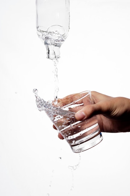 Photo close-up of hand pouring water from glass against white background