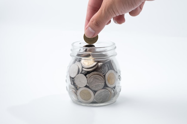 close-up of hand putting coin into jar against white background