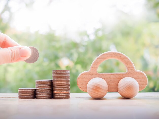 Close up of hand putting coins in stack of coins and wooden toy car for transport and manage success business concept Concept of car loan