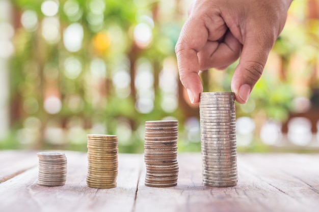 Close up hand putting coins in stack on wooden plank. savings concept.