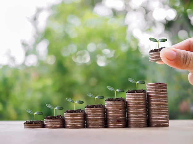 Photo close up hand putting coins with plants growing up on stack of coins the concept of saving money financial investment and business growing