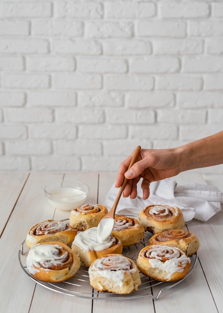 Close up hand putting cream on cinnamon rolls