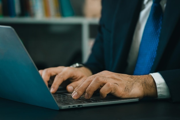 Close up hand's business man wearing suit typing and working on laptop computer on wooden table at home office Entrepreneur man working for business at home office Working technology concept