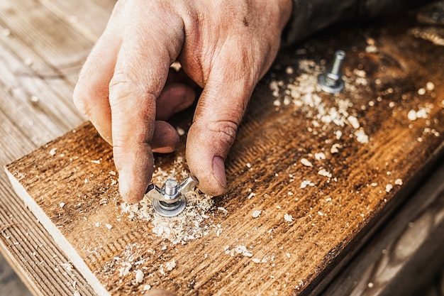 Foto stretta di mano avvitando un bullone in una tavola di legno