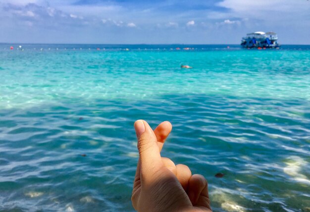 Photo close-up of hand over sea against blue sky