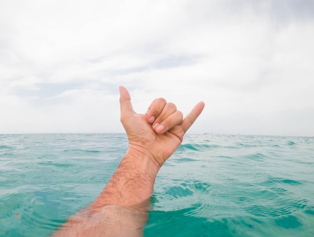 Close-up of hand over sea against sky