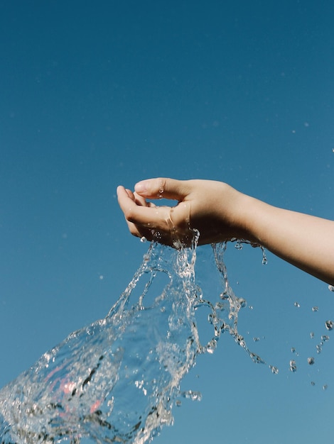 Foto close-up di una mano che spruzza acqua contro un cielo blu limpido