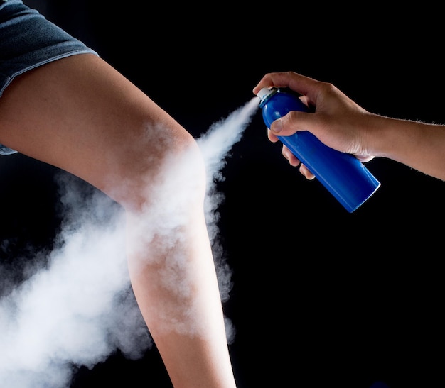 Photo close-up of hand spraying medicine on leg over black background