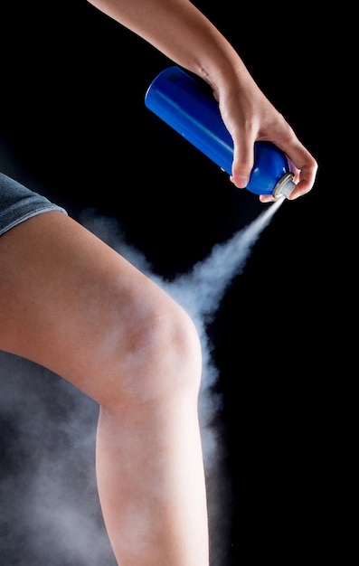 Close-up of hand spraying medicine on leg over black background