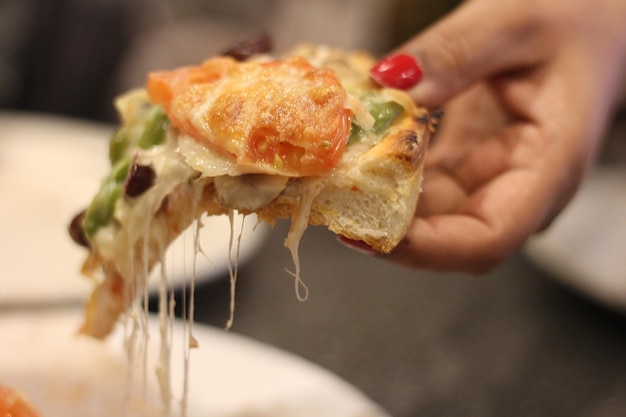 Foto close-up della mano che prende una fetta di pizza dal piatto