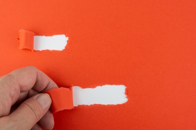 Photo close-up of hand tearing orange paper on wall