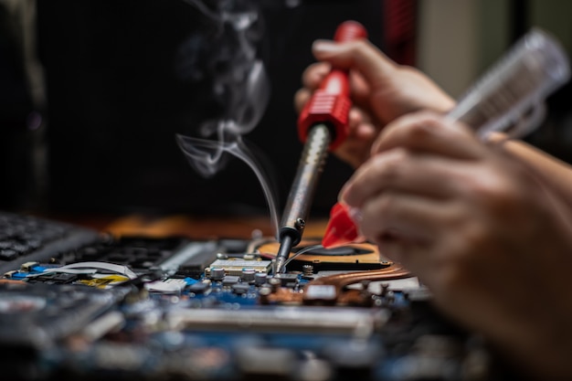 Close-up hand technician repairing broken laptop notebook computer with electric soldering Iron