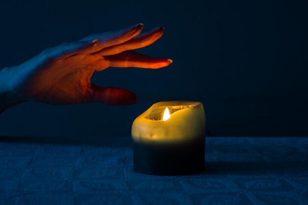 Close-up of hand touching burning candle