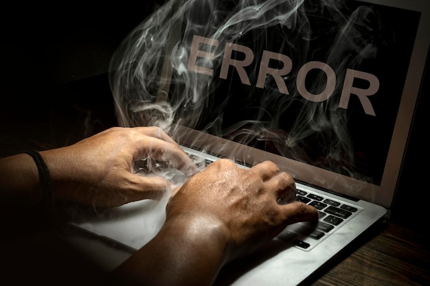 Photo close up hand typing a laptop burned with smokes on a wooden desk isolated over black background