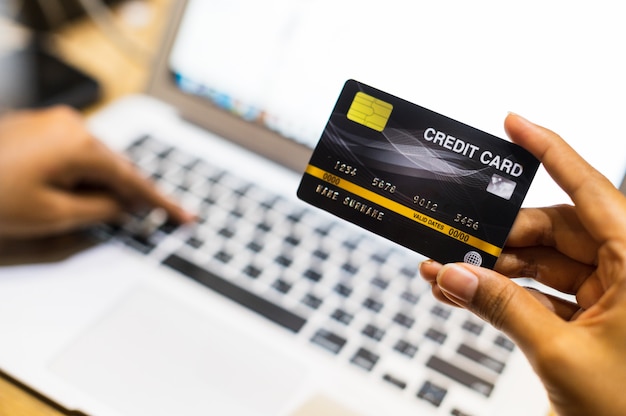 Chiuda sulla mano facendo uso della carta di credito che compera online, concetto cashless