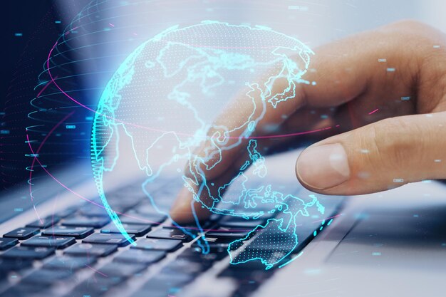 Close up of hand using laptop at desktop with glowing digital blue globe hologram on blurry background Internet earth and future concept Double exposure