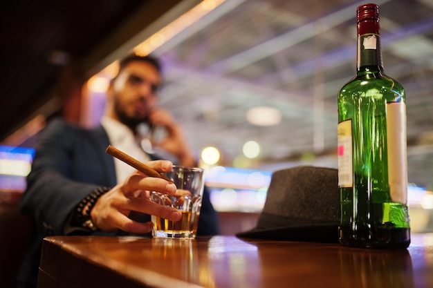 Close-up hand van knappe, goedgeklede Arabische man met glas whisky en sigaar geposeerd in pub