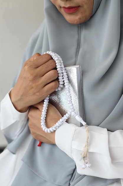 Close-up hand van moslimvrouw die hijab draagt met gebedsbonen of tasbeeh en heilig boek van de koran