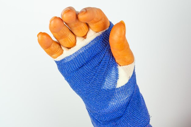 Close-up of hand with bandage against white background