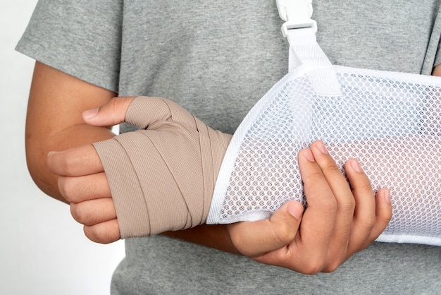 男の腕の怪我の概念と包帯の手腕のスリングとして白い背景に包帯分離で手を閉じます。