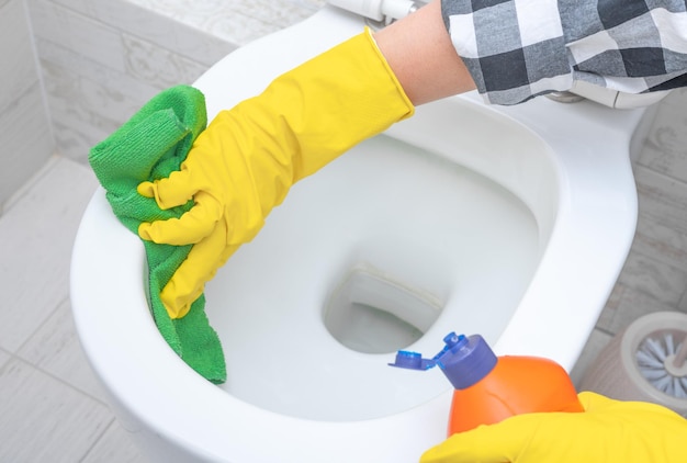 Chiudere la mano con il detergente per la pulizia della toilette servizio di pulizia mani che indossano guanti protettivi gialli utilizzando una soluzione detergente liquida per la pulizia della toilette a filo e il concetto di igiene