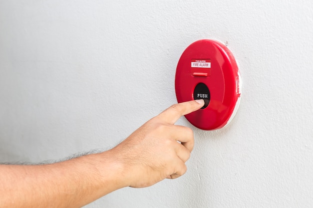 Foto chiuda sulla mano con il dito che preme l'allarme antincendio rosso sulla parete