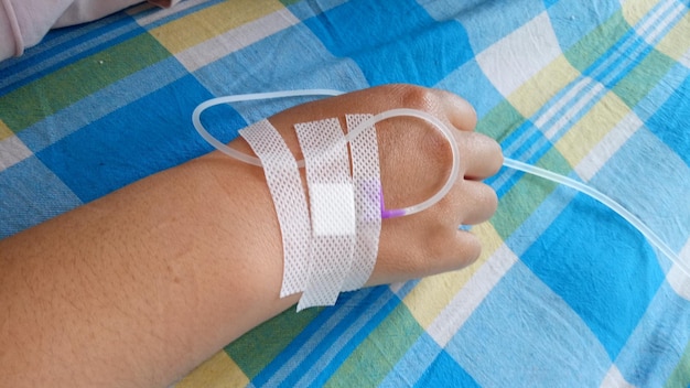 Photo close-up of hand with iv drip on bed at hospital