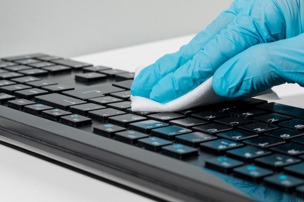 Photo close-up of hand with surgical glove disinfecting keyboard