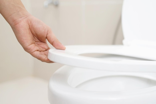 Close up hand of a woman closing the lid of a toilet seat Hygiene and health care concept